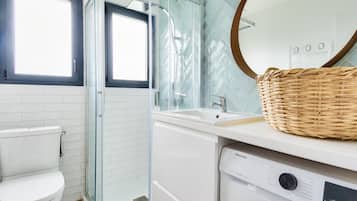A modern bathroom with a glass shower enclosure, a white toilet, and a washing machine.
