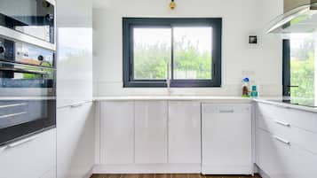 A modern kitchen with white cabinets, a dishwasher, and a window with a view of greenery.