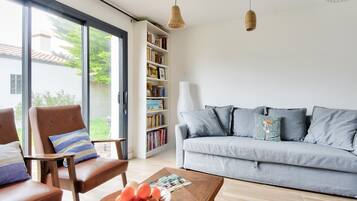 A modern living room with a grey sofa, a wooden coffee table with a bowl of fruit, and a bookshelf filled with books.