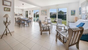 A spacious living area with a dining set, a sofa, and a large window offering a view of the garden. - 50m from the beach, house with garden for 10 (Piriac-sur-Mer)