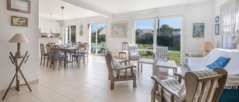 A spacious living area with a dining set, a sofa, and a large window offering a view of the garden.