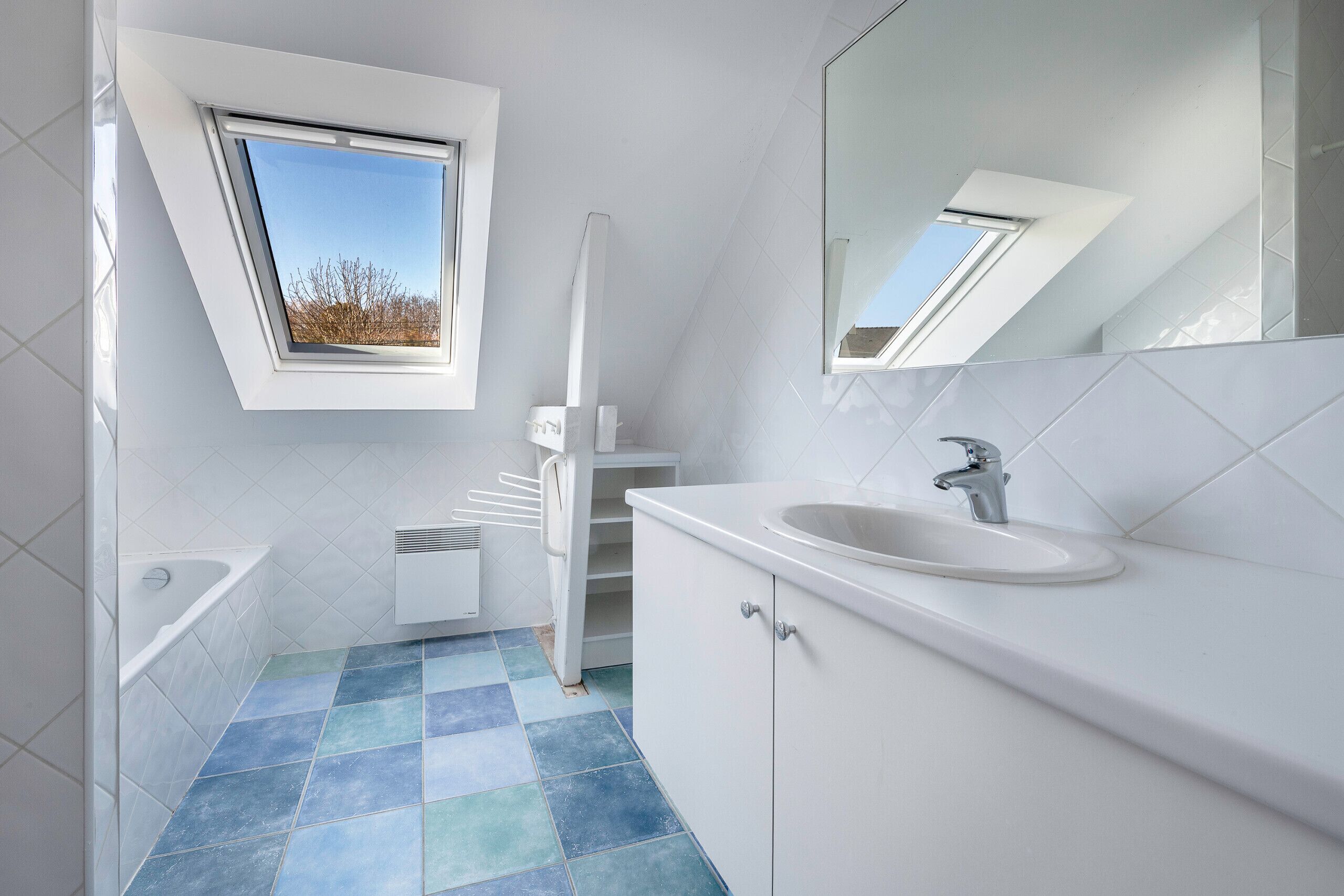 Un baño moderno con tragaluz, azulejos blancos, una bañera y un lavamanos.