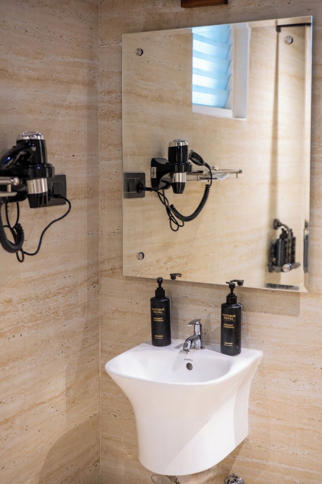 A bathroom with a white sink, two black toiletries, a hairdryer, and a mirror.