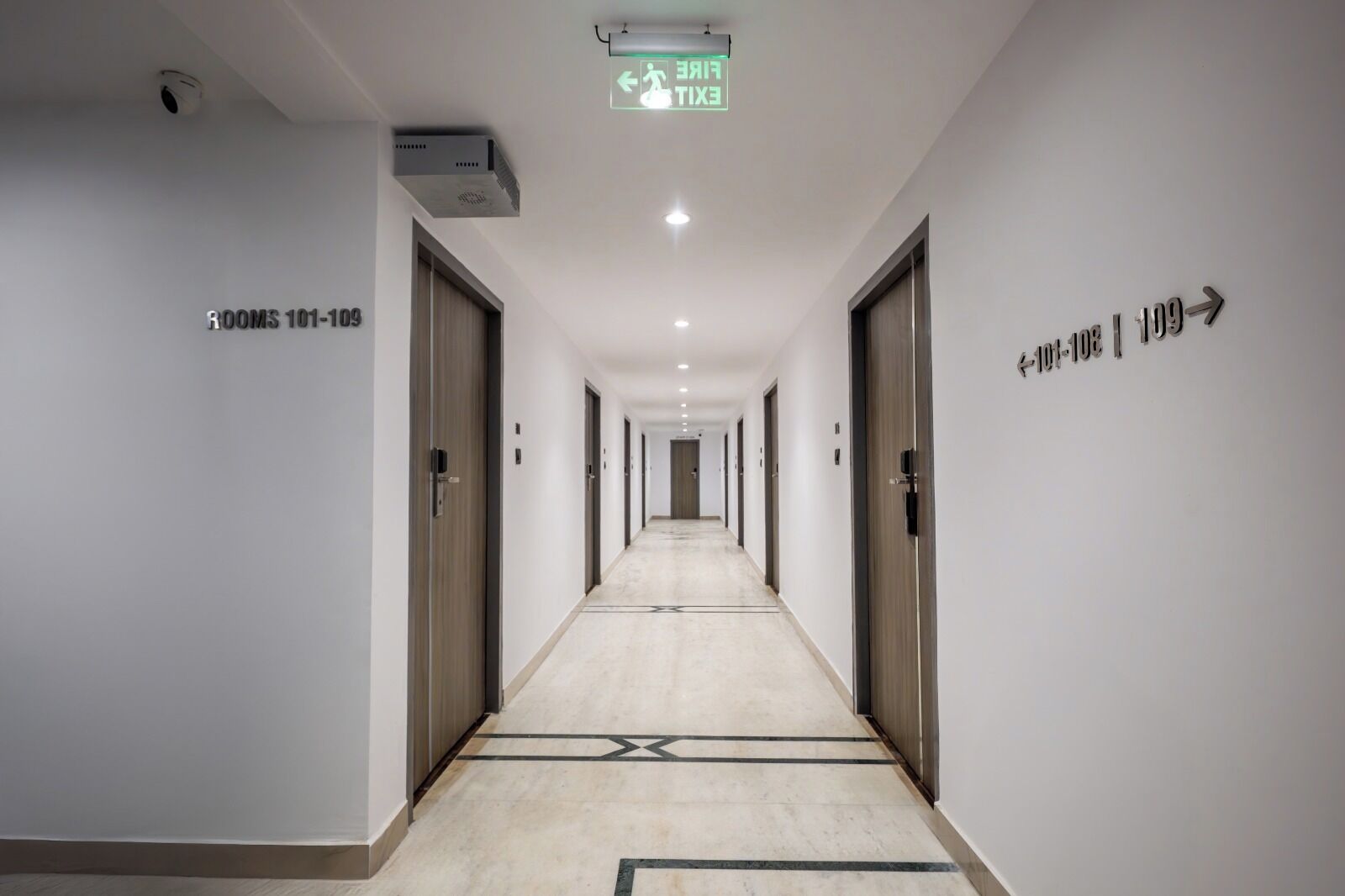 Un pasillo de hotel con puertas identificadas como 'Habitaciones 101-109' y un letrero de salida.