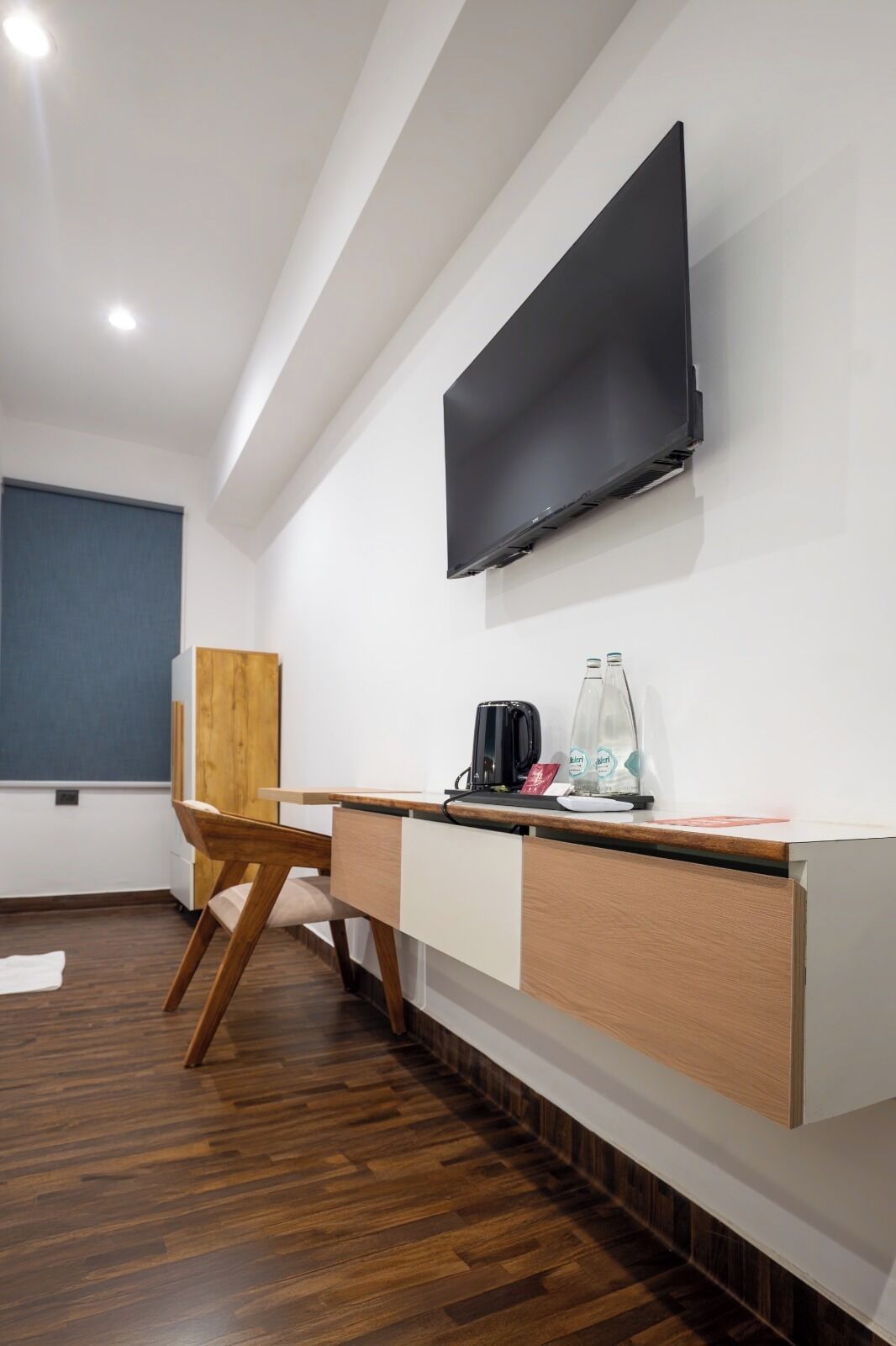 A modern room with a wooden desk, a flat-screen TV mounted on the wall, and a wooden chair.