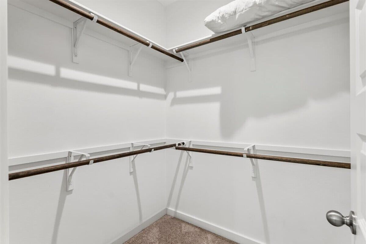 A corner closet with white walls, a wooden door, and a white door handle.