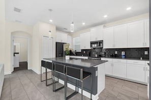 A modern kitchen with white cabinets, a large island, and bar stools.