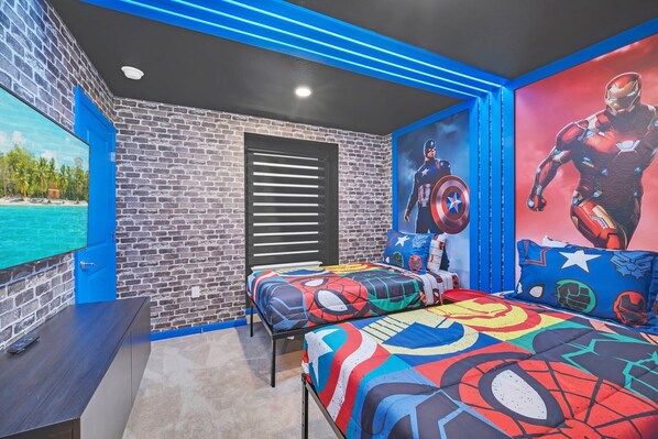 Ein Zimmer mit Ziegelwand, einem Bett mit farbenfroher Spider-Man Bettdecke, einem großen Captain America Poster und einem Fernseher links.