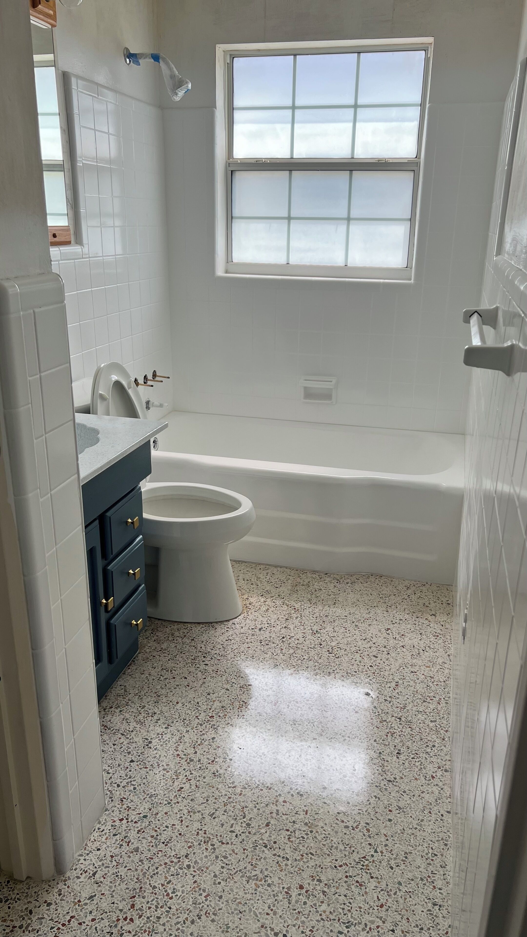 Un baño con azulejos blancos, una bañera, un inodoro y una ventana.
