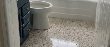 Un baño con azulejos blancos, una bañera, un inodoro y una ventana.