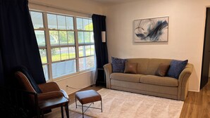 Un salon avec un canapé, deux fauteuils, un tapis et une fenêtre avec des rideaux.