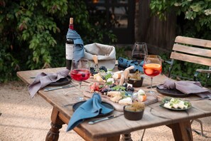 Et udendørs træbord dækket med vin, glas, ost, oliven og brød.