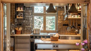 Een keuken met een houten aanrecht, een fornuis en hangende pannen. Er is een raam met uitzicht op bomen.