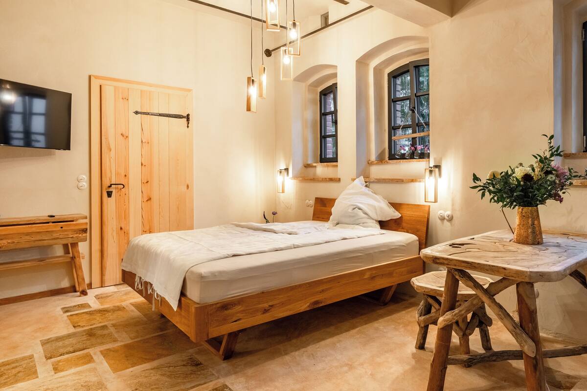 Un dormitorio con cama de madera, mesita de noche, televisor montado en la pared y ventana con vistas.