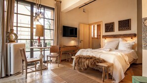 Een slaapkamer met een groot bed, een bureau, een stoel, een televisie en een raam met gordijnen.