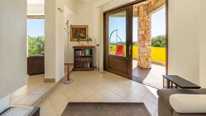 Una sala de estar moderna con un sofá, una mesa de centro, una estantería y vistas a un balcón con pared amarilla y vegetación.