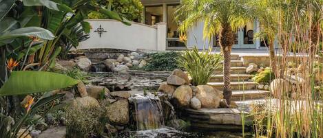 A garden with a pond, stone steps, and tropical plants.