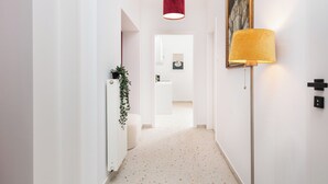 A hallway with a white radiator, a potted plant, a red pendant light, a yellow floor lamp, and a framed picture on the wall. - Retro Glamour by Upstairs (Kraków)
