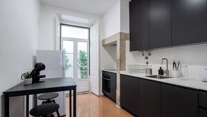 A modern kitchen with dark cabinets, a white countertop, and a small dining area with a table and stools. - Rosemary Apartment, Campo de Ourique, Lisbon (Lisboa)
