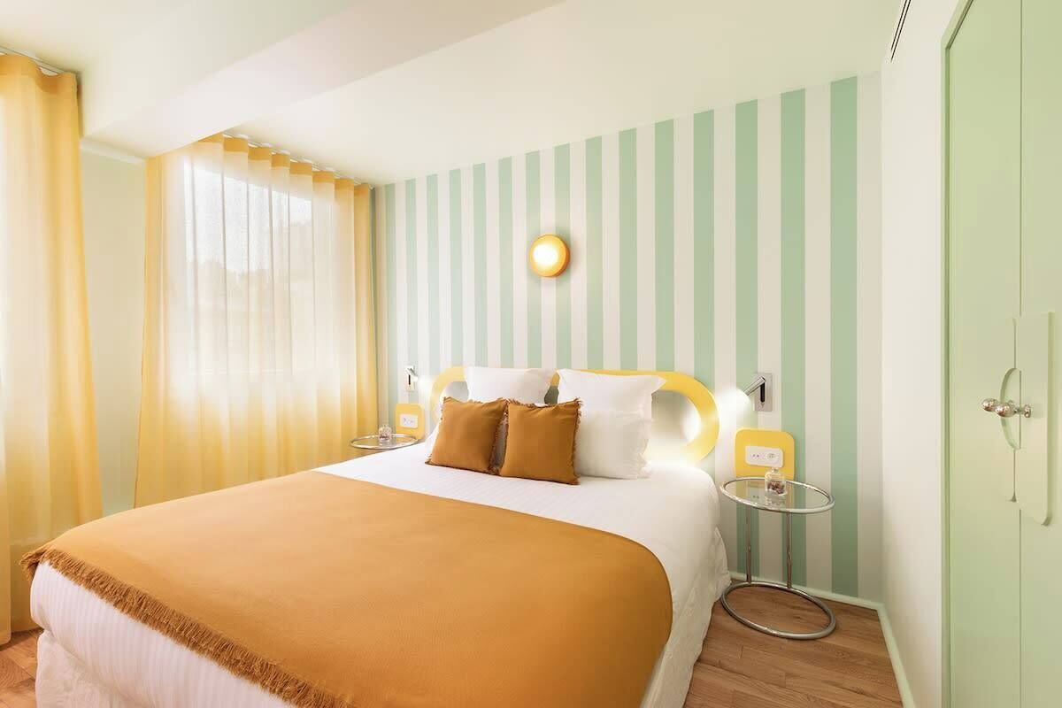 Een hotelkamer met een bed, nachtkastje, lamp en een wandlamp.