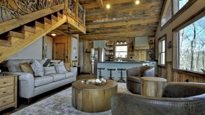L’intérieur d’un chalet rustique comprend un escalier en bois, un canapé, une table basse ronde et un coin cuisine.