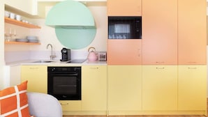 A compact kitchen with a modern design, featuring a built-in oven, a coffee maker, and a kettle on the countertop.