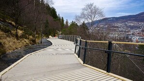 A wooden boardwalk with a metal railing, surrounded by trees and a view of a city in the distance. - Spacious near-city villa with amazing views, 5BR, Free Parking (Vestland)
