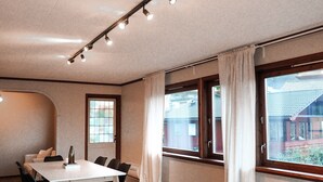 A modern living room with a white sofa, a dining table with chairs, and large windows with curtains. - Spacious near-city villa with amazing views, 5BR, Free Parking (Vestland)
