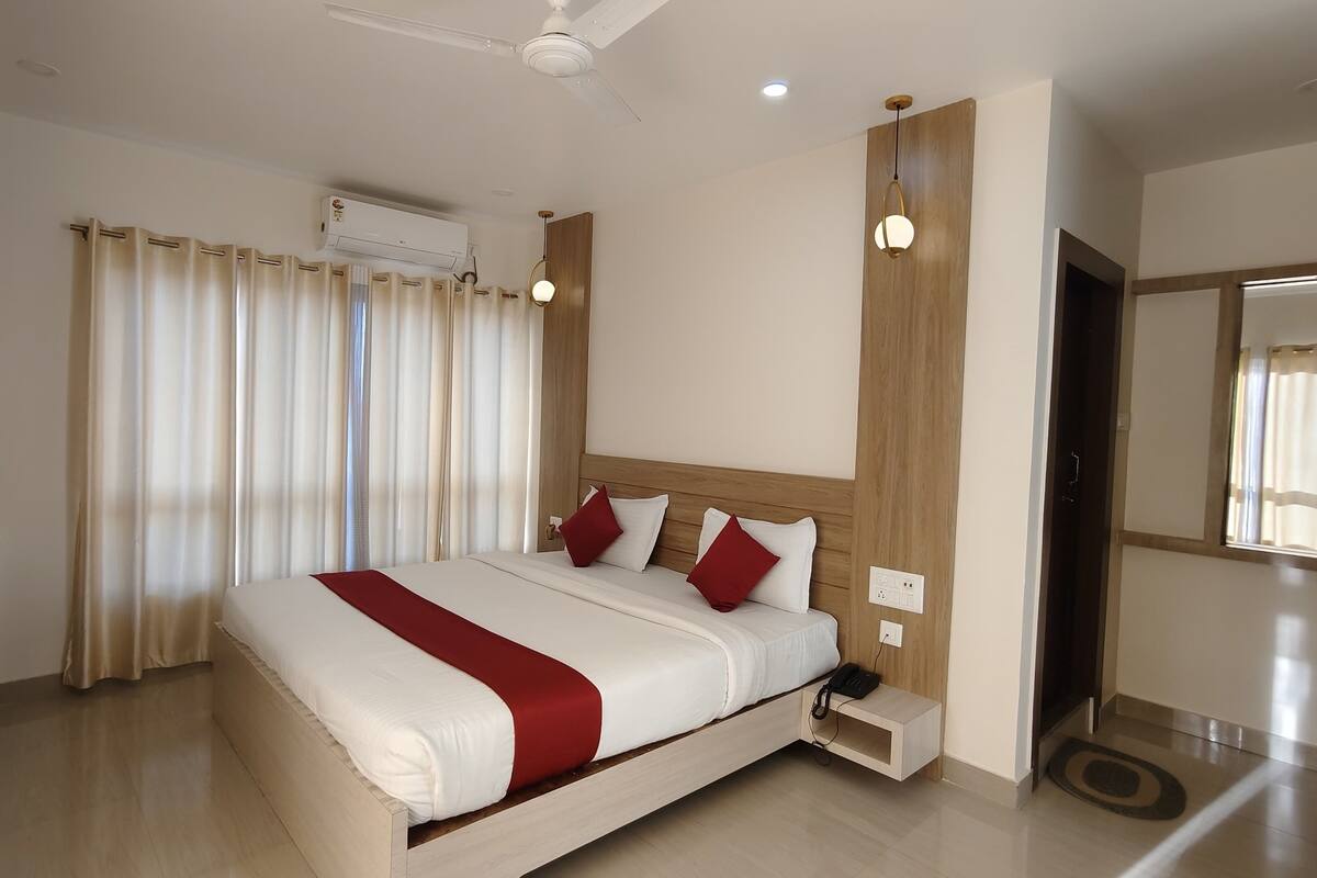 A modern hotel room with a large bed, a flat-screen TV, a desk with a keyboard, and an air conditioning unit.