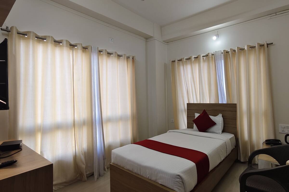 A hotel room with a bed, a desk with a laptop, a chair, and curtains.
