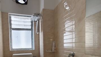 A bathroom with a toilet, sink, shower, and a window.