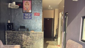 A reception area with a marble reception desk, a digital clock, a no smoking sign, and a no drinking sign. There are two sofas and a small table in the seating area. - HOTEL LA PLAZO (Haridwar)