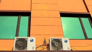 A multi-story building with orange and green window frames, air conditioning units, and a clear blue sky. - HOTEL LA PLAZO (Haridwar)