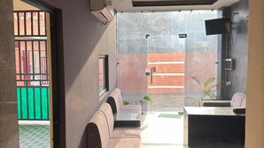 A hotel lobby with a sofa, a small table, and a TV mounted on the wall. - HOTEL LA PLAZO (Haridwar)