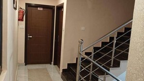 A hallway with a marble floor, a wooden door labeled "202", and a staircase with metal railings. - HOTEL LA PLAZO (Haridwar)