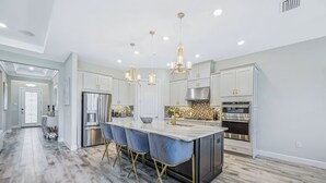 A modern kitchen with a central island, stainless steel appliances, and pendant lighting. - Esplanade by the Islands (Naples)