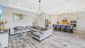 A modern living room with a sectional sofa, a dining area with bar stools, and a kitchen with stainless steel appliances. - Esplanade by the Islands (Naples)