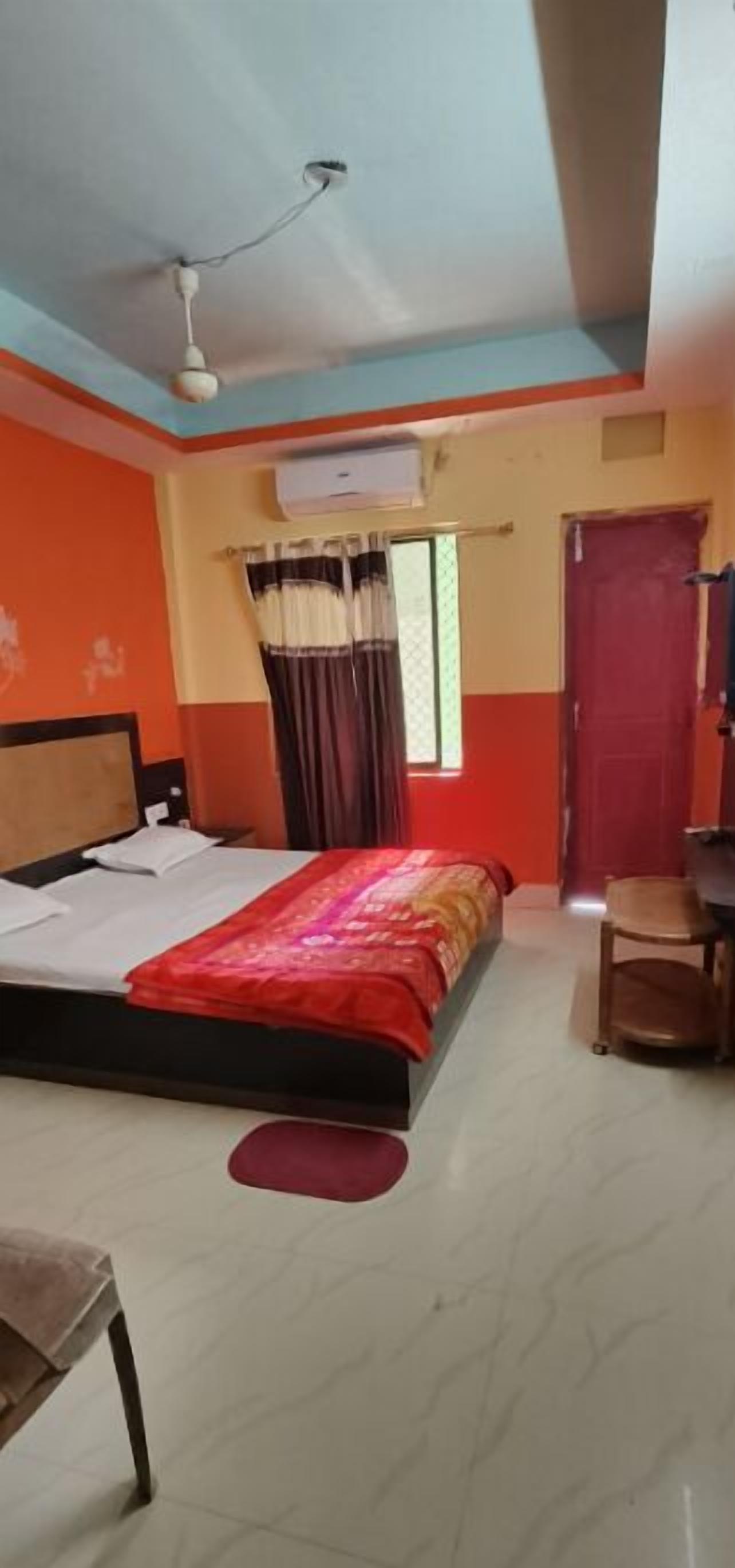 A hotel room with a bed, a chair, an air conditioning unit, and a window with curtains.