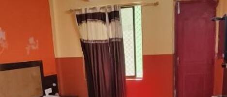 A hotel room with a bed, a chair, an air conditioning unit, and a window with curtains.