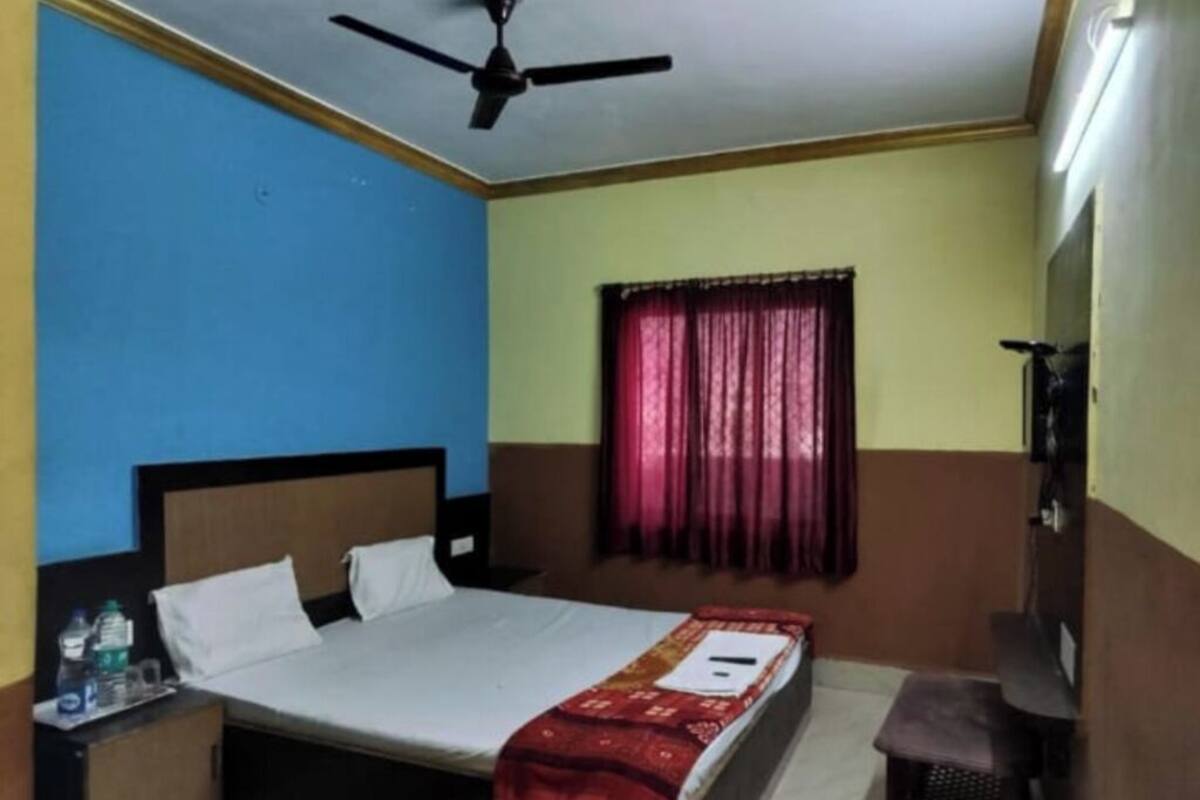 A hotel room with a bed, a nightstand, a desk, a chair, a ceiling fan, and a window with curtains.