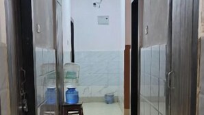 Un couloir avec un sol carrelé, un distributeur d’eau et un petit tabouret.