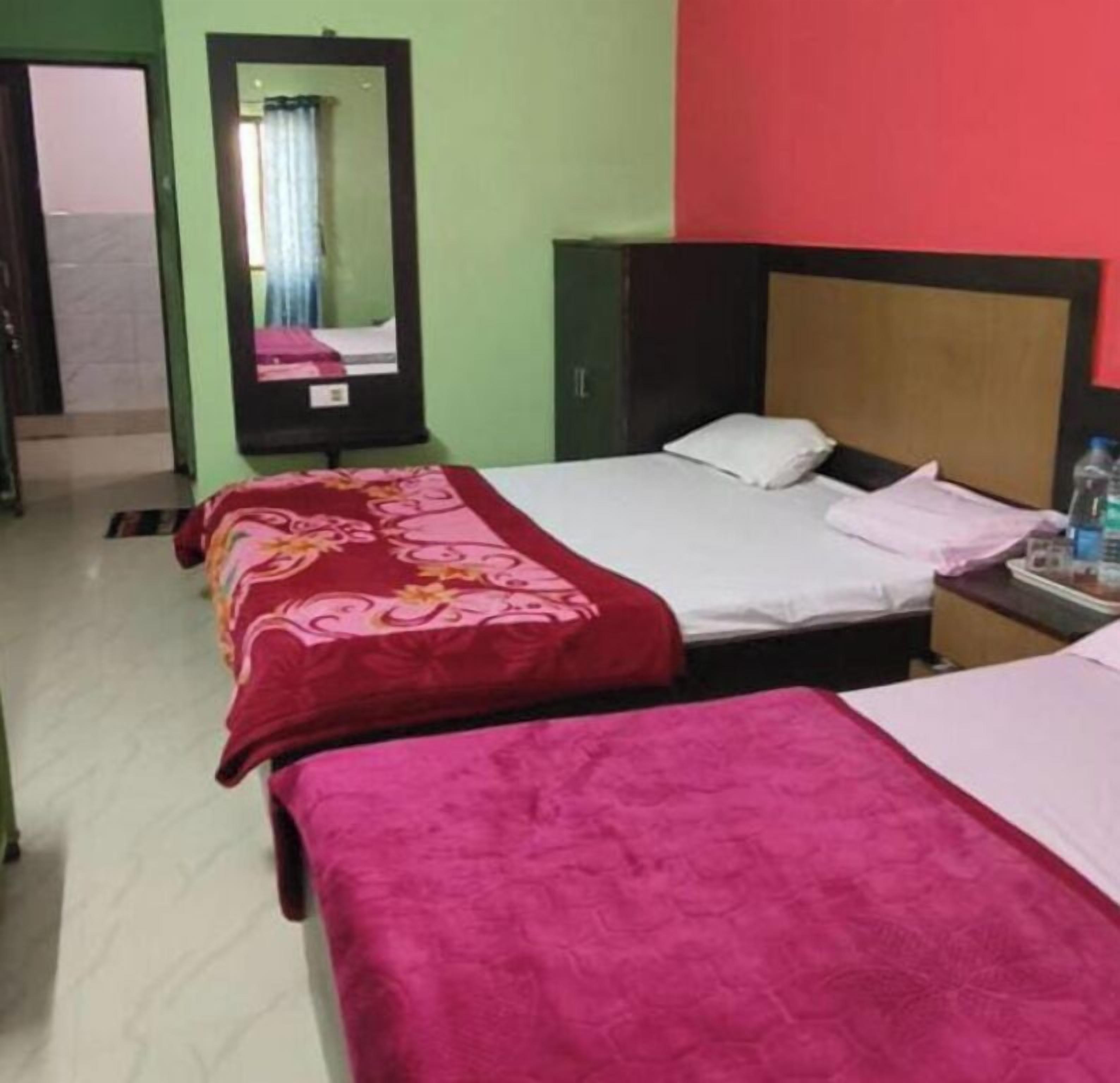 A hotel room with two beds, each with a red bedspread and white pillows. There is a nightstand with a water bottle and a lamp.