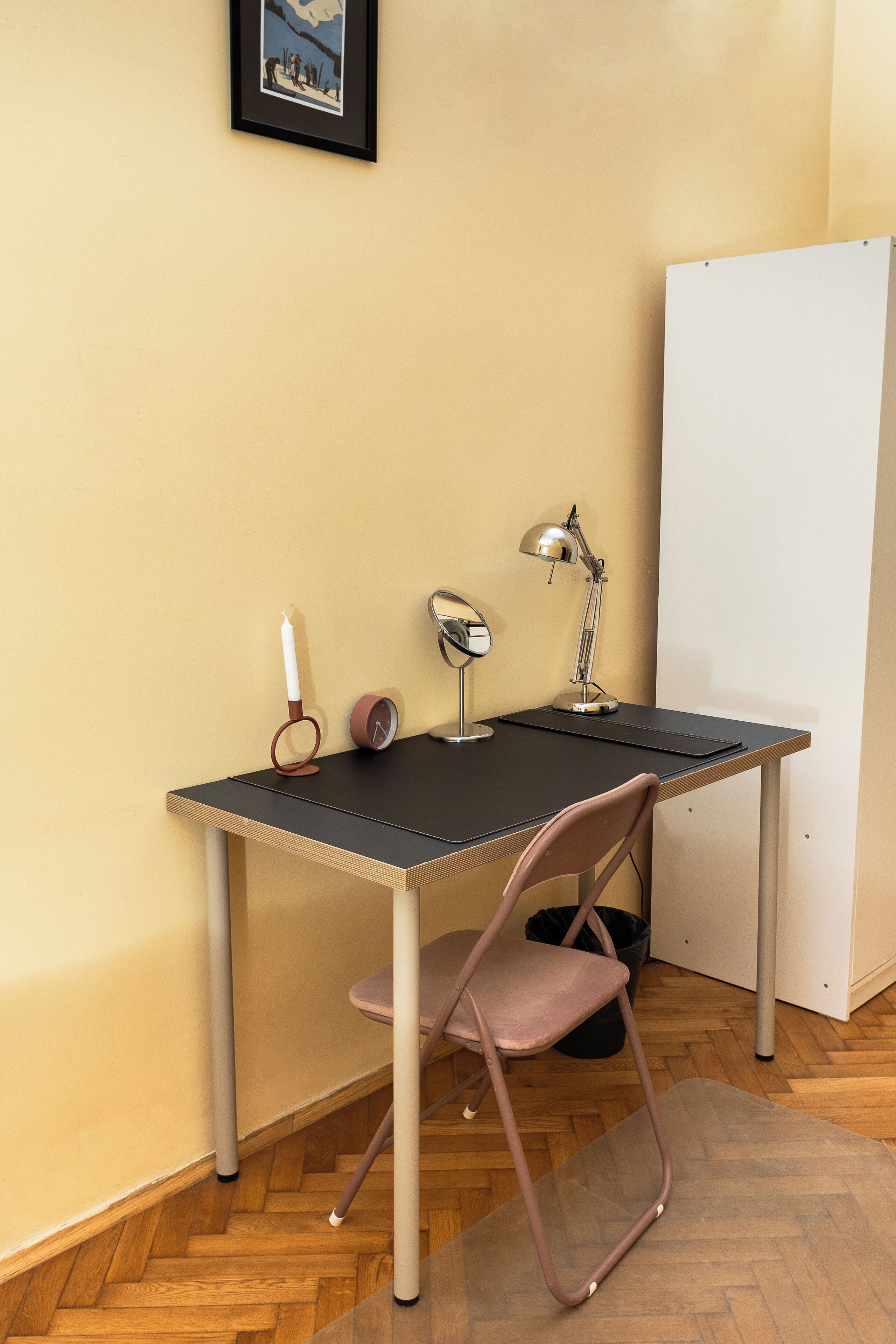 Un petit espace de travail comprenant un bureau, une chaise, une lampe de bureau et un tableau encadré accroché au mur.