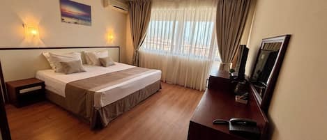 A hotel room with a bed, bedside tables, a desk with a telephone, a mirror, and a window with curtains.