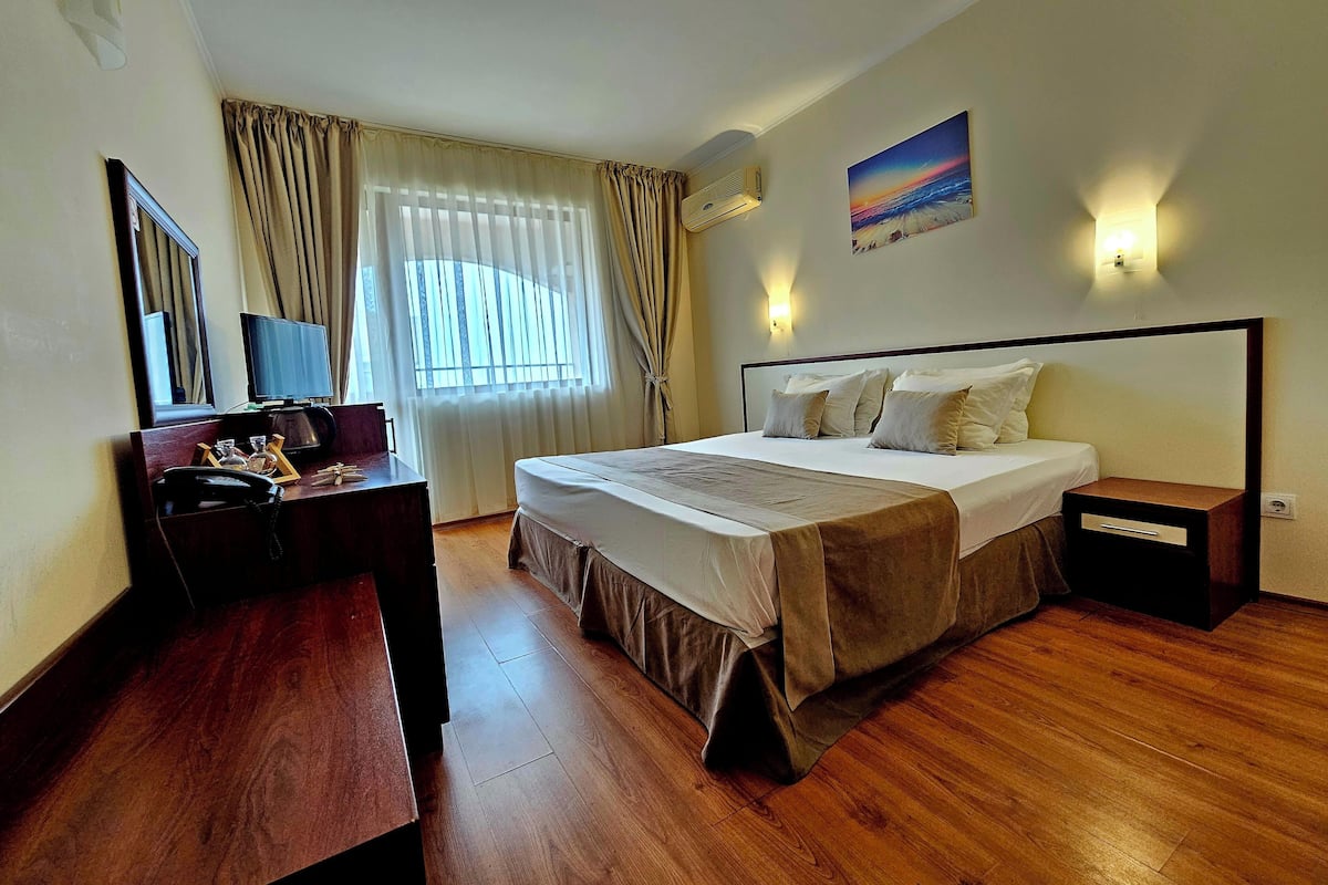 Una habitación de hotel con cama, mesita de noche, escritorio y teléfono, y una ventana con cortinas.