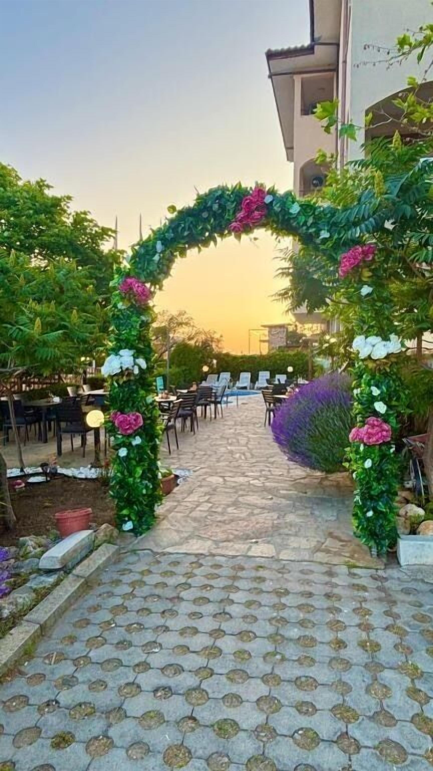 An outdoor seating area with a stone pathway leading to a covered entrance decorated with greenery and flowers.