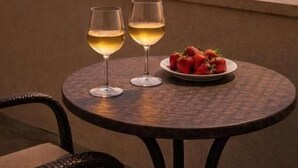 A round table with two wine glasses and a plate of strawberries, overlooking a sunset over the sea with buildings in the background. - Sea Vista Hotel (Sveti Vlas)