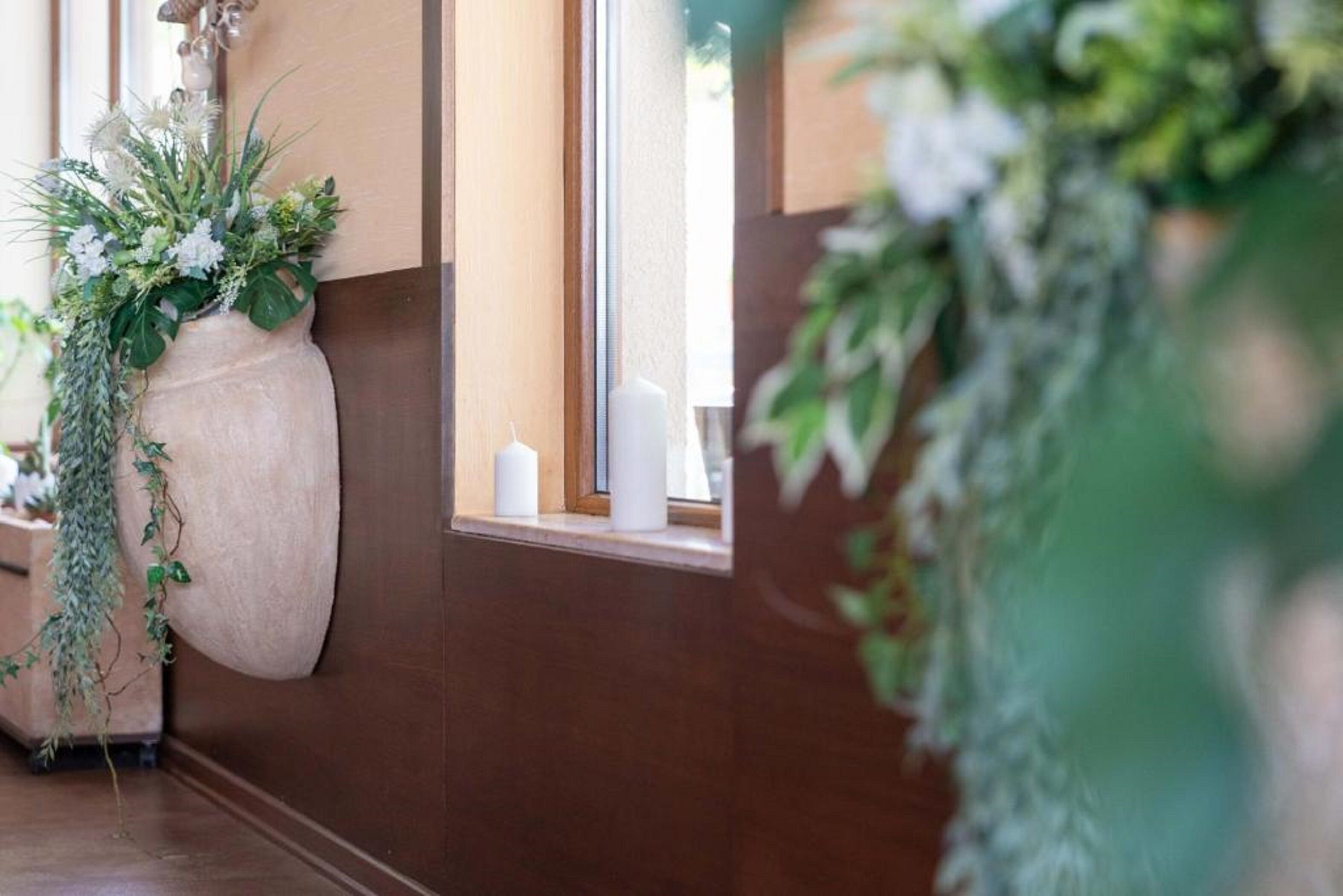 A bathroom with a large vase of flowers, a window with a view, and a mirror.