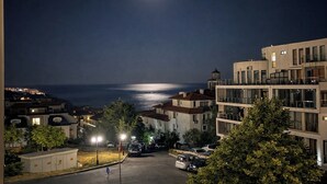 A nighttime view of a coastal residential area with buildings, a street, and a body of water under a moonlit sky. - Sea Vista Hotel (Sveti Vlas)