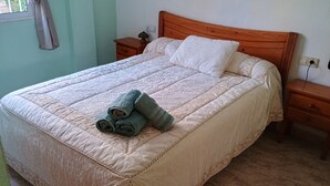Un llit ben fet amb un estovat beix, dos coixins i tres tovalloles arremolinades. Hi ha dues mesetes de nit de fusta, amb una làmpada sobre una d'elles.